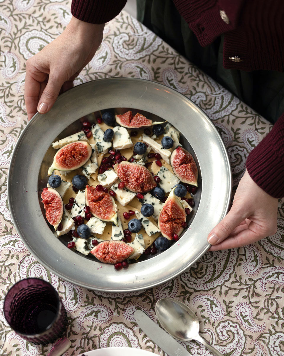 Winterliche Käseplatte mit Blauschimmelkäse, frischen Feigen, Brombeeren und Granatapfelkernen auf einer silberfarbenen Servierplatte – angerichtet auf der Blockprint-Tischdecke „Purple Paisley“.